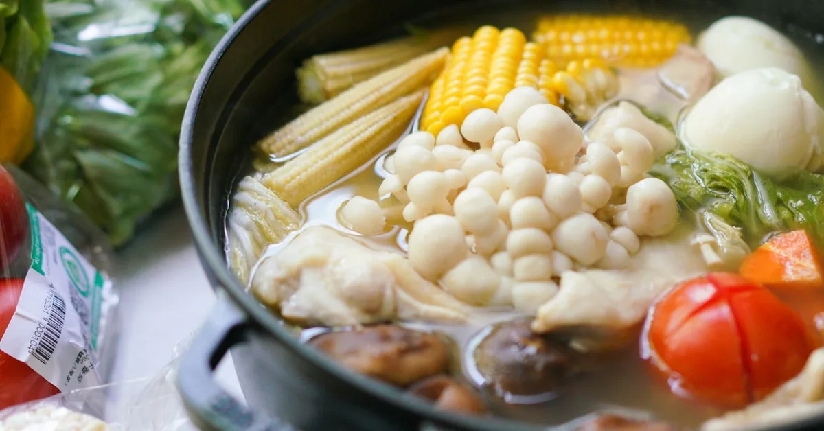 Uma panela de cozido quente fumegante com carne e legumes cozidos sobre a mesa de madeira.