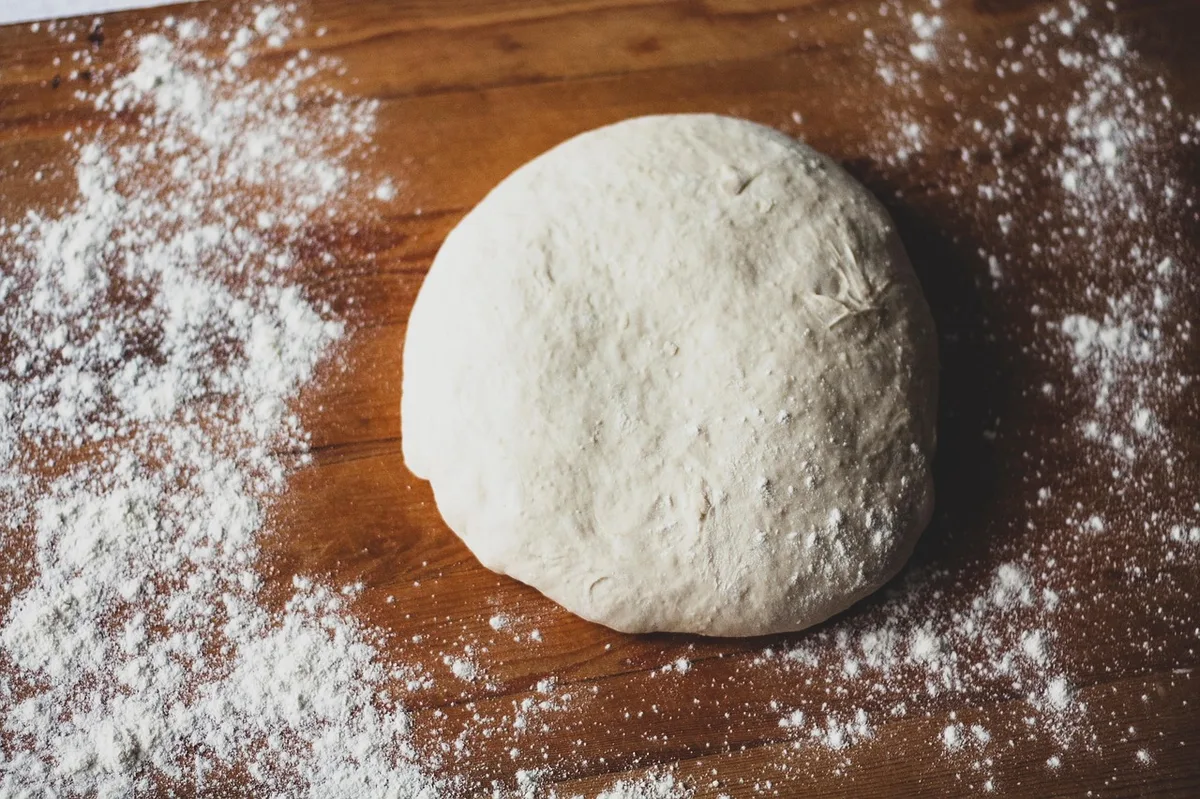 Massa de pão fresca sendo sovada com rolo sobre bancada de madeira