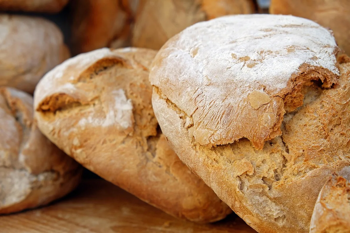 Pão caseiro polvilhado com farinha sobre superfície de madeira
